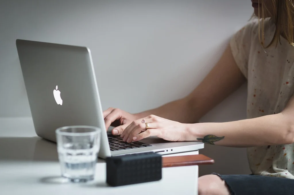 Person arbeitet im Homeoffice an einem Laptop mit einem Glas Wasser auf dem Schreibtisch